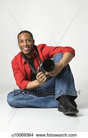 Picture - African American young male adult sitting on floor with camera looking at viewer smiling.. Fotosearch