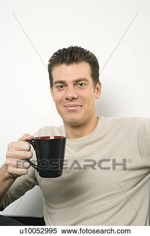 Stock Photography - Caucasian mid-adult man holding coffee cup and looking at viewer.. Fotosearch