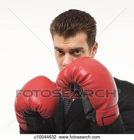 Stock Image - Caucasian mid-adult man wearing suit and holding boxing gloves close to his face.. Fotosearch