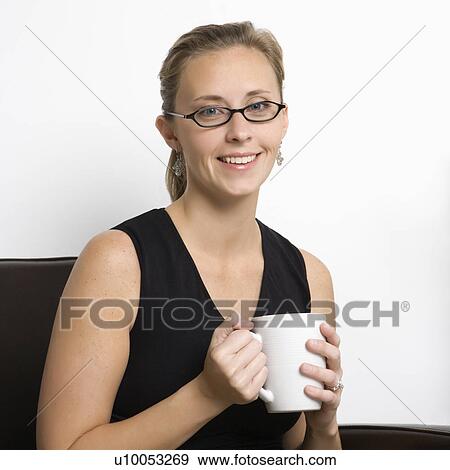 Stock Photo - Caucasian mid-adult woman wearing eyeglasses holding coffee cup and looking at viewer.. Fotosearch