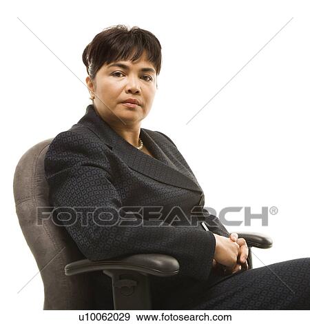 Stock Photo - Filipino middle-aged businesswoman sitting in office chair against white background.. Fotosearch