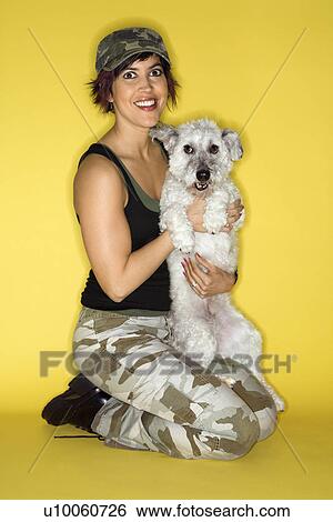 Stock Photograph - Hispanic mid-adult woman kneeling holding small white dog.. Fotosearch
