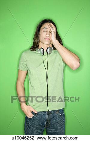 Portrait of Asian-American teen boy with headphones around neck and hand on forehead standing against green background. View Large Photo Image Stock Image - Portrait of Asian-American teen boy with headphones around neck and hand on forehead standing against green background.. Fotosearch