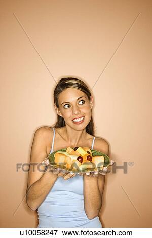 Portrait of young adult woman holding a plate of fruit. View Large Photo Image Stock Photo - Portrait of young adult woman holding a plate of fruit.. Fotosearch