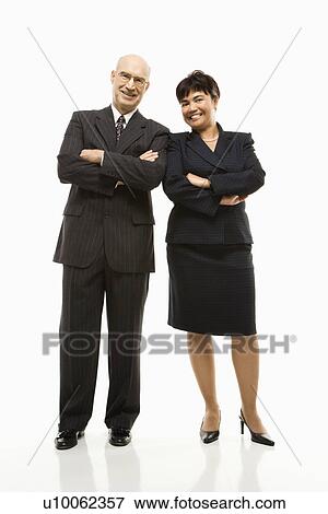 Stock Photo - Smiling Caucasian middle-aged businessman and Filipino businesswoman standing with arms crossed against white background.. Fotosearch