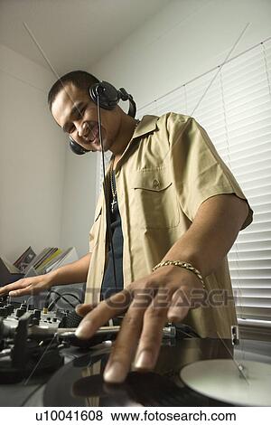 Stock Photo - Asian young adult male DJ standing with hand on spinning record on turntable and smiling.. Fotosearch