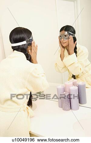Asian/Indian young woman looking in mirror adjusting eye mask. View Large Photo Image Stock Photograph - Asian/Indian young woman looking in mirror adjusting eye mask.. Fotosearch