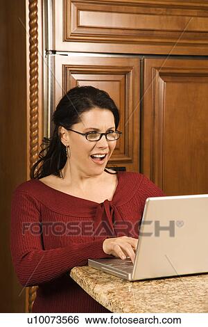 Caucasian woman typing on laptop in kitchen and looking at monitor with shocked expression. View Large Photo Image Stock Photograph - Caucasian woman typing on laptop in kitchen and looking at monitor with shocked expression.. Fotosearch