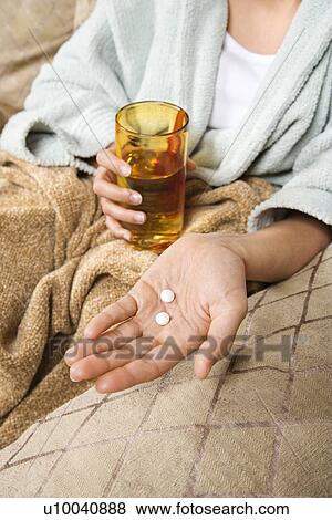 Stock Photo - Caucasian/Hispanic young woman holding pills in hand with glass of water.. Fotosearch