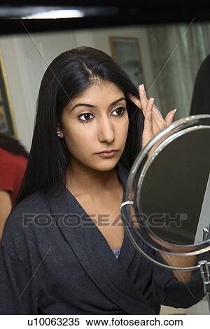 Stock Photography - Close up of Asian/Indian young woman looking in mirror primping.. Fotosearch