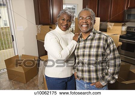 Stock Photography - Portrait of middle-aged African-American couple in kitchen with moving boxes.. Fotosearch