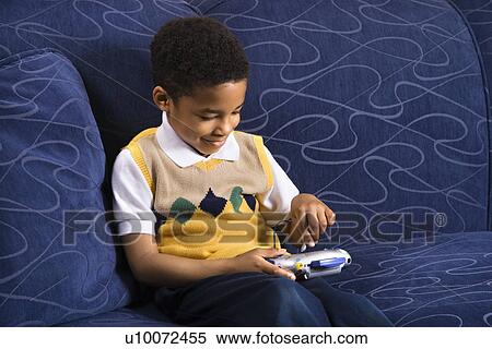 Stock Photography - Portrait of young boy playing video game on couch. . Fotosearch