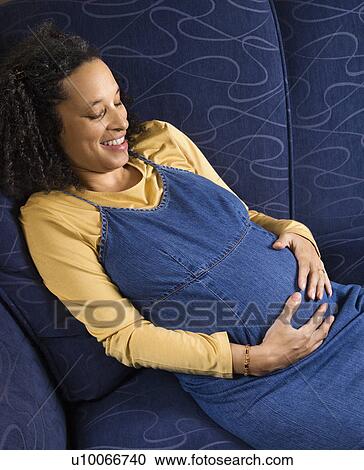 Stock Image - Portrait of young pregnant female with hands on stomach.. Fotosearch