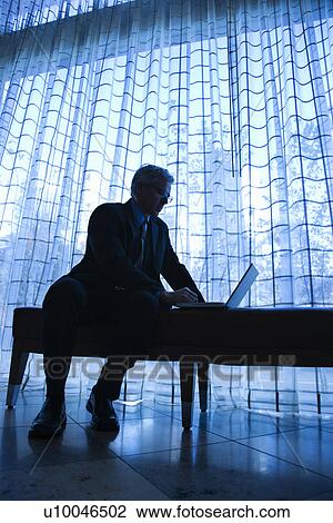 Blue tone silhouetted image of prime adult Caucasian man in suit sitting on bench typing on laptop. View Large Photo Image Stock Image - Blue tone silhouetted image of prime adult Caucasian man in suit sitting on bench typing on laptop.. Fotosearch