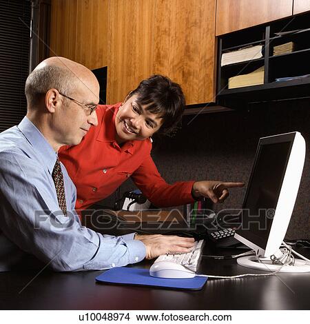 Businessman and businesswoman in office smiling looking and pointing at computer monitor. View Large Photo Image Picture - Businessman and businesswoman in office smiling looking and pointing at computer monitor.. Fotosearch