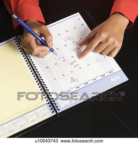 Stock Image - Businesswoman writing in appointment calendar.. Fotosearch