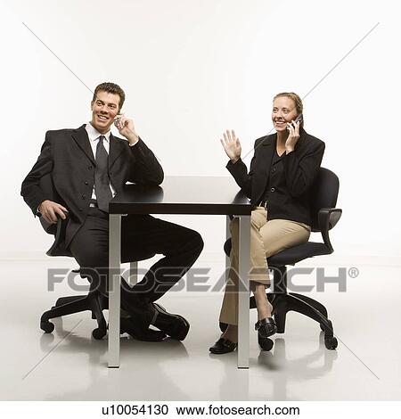 Stock Image - Caucasian mid-adult businessman and woman smiling while sitting and talking on cell phones.. Fotosearch