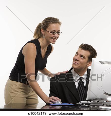 Stock Photo - Caucasian mid-adult woman touching mid-adult man's shoulder and using mouse at computer.. Fotosearch