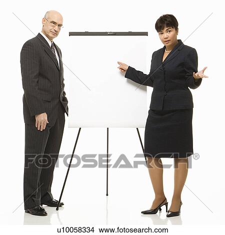 Picture - Caucasian middle-aged businessman and Filipino businesswoman standing making presentation against white background.. Fotosearch