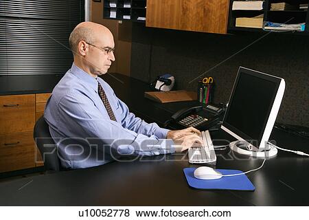 Caucasian middle-aged businessman sitting at desk in office typing on computer. View Large Photo Image Stock Photo - Caucasian middle-aged businessman sitting at desk in office typing on computer.. Fotosearch