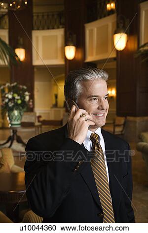 Caucasian prime adult male businessman talking on cellphone in hotel lobby. View Large Photo Image Stock Image - Caucasian prime adult male businessman talking on cellphone in hotel lobby.. Fotosearch