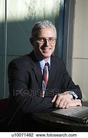 Close up of prime adult Caucasian man in suit sitting at table with laptop looking at viewer and smiling. View Large Photo Image Stock Image - Close up of prime adult Caucasian man in suit sitting at table with laptop looking at viewer and smiling.. Fotosearch