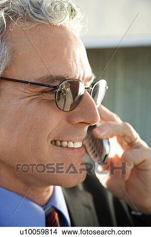 Picture - Close up profile of prime adult Caucasian man in suit smiling and talking on cellphone in urban setting.. Fotosearch