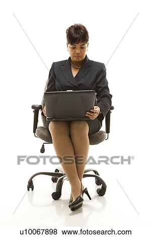 Stock Photo - Filipino middle-aged businesswoman sitting in office chair with laptop against white background.. Fotosearch