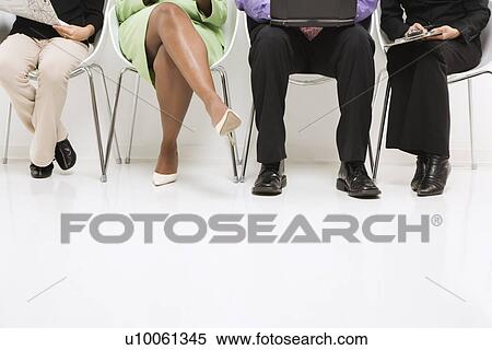 Stock Photography - Legs of multi-ethnic business group of men and women sitting with laptop and papers.. Fotosearch