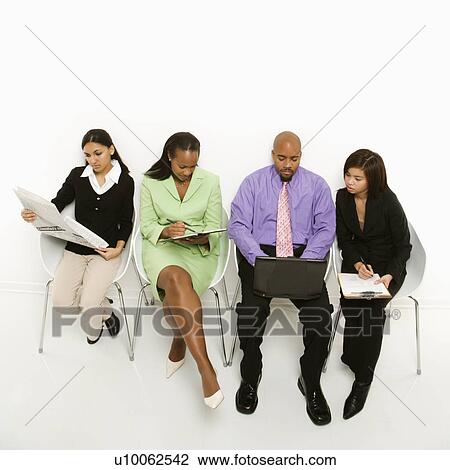 Stock Image - Multi-ethnic business group of men and women sitting looking at laptop and papers.. Fotosearch
