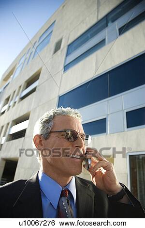 Stock Photograph - Prime adult Caucasian man in suit smiling and talking on cellphone in urban setting.. Fotosearch