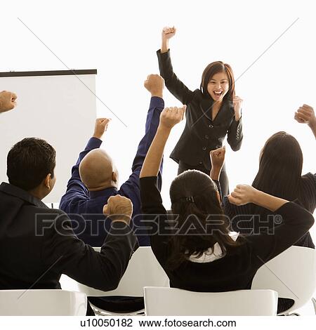 Stock Image - Vietnamese mid-adult woman standing in front of cheering business group during a presentation.. Fotosearch