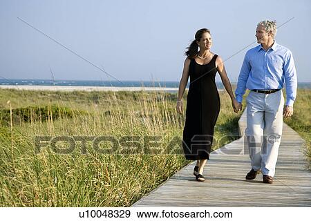 Stock Photo - Caucasian mid-adult couple holding hands and walking on walkway.. Fotosearch