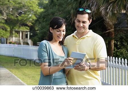 Stock Image - Mid-adult Caucasian couple holding a map and smiling.. Fotosearch