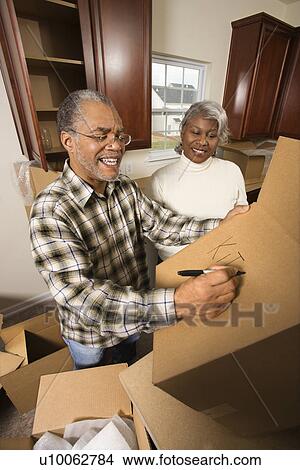 Middle-aged African-American male labeling moving box with wife in background. View Large Photo Image Picture - Middle-aged African-American male labeling moving box with wife in background.. Fotosearch