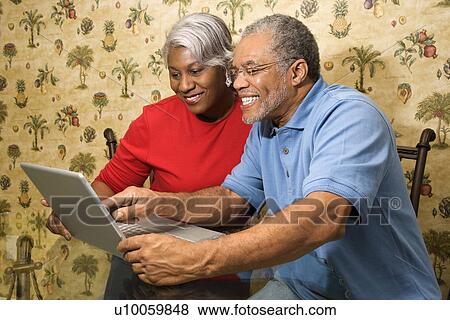 Portrait of mature African American couple looking at laptop in home. View Large Photo Image Stock Photo - Portrait of mature African American couple looking at laptop in home. . Fotosearch