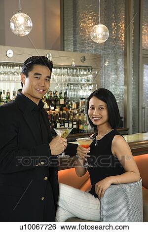 Stock Photograph - Prime adult Asian male and female at bar with cocktails.. Fotosearch