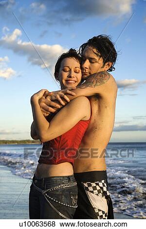 Stock Photo - Young Caucasian adult couple embracing on beach.. Fotosearch