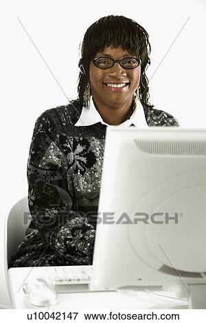 Stock Photo - African-American mid-adult woman wearing headset typing on computer.. Fotosearch