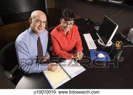 Stock Photograph - Businessman and businesswoman in office smiling going over appointment calendar.. Fotosearch