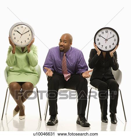Stock Image - Businesswomen sitting holding clocks over faces while African-American businessman shrugs.. Fotosearch