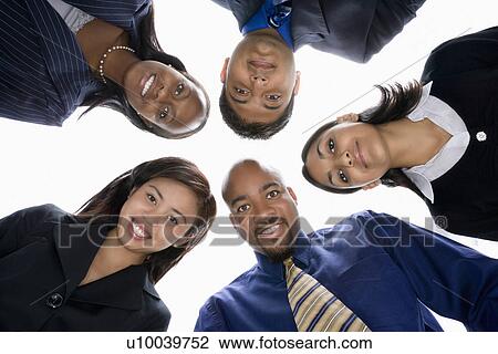 Stock Image - Low angle portrait of multi-ethnic business group of men and women in huddle looking at viewer.. Fotosearch