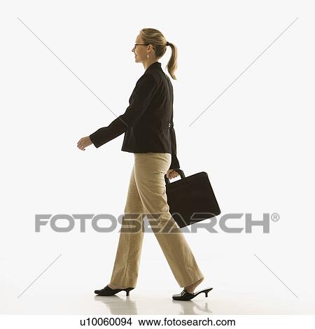 Picture - Mid-adult Caucasian businesswoman walking and carrying briefcase.. Fotosearch