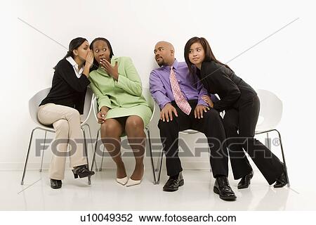 Stock Image - Multi-ethnic businesswomen whispering and making faces while colleagues eavesdrop.. Fotosearch