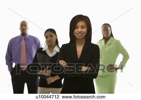 Stock Image - Portrait of Vietnamese businesswoman smiling with arms crossed with others in background.. Fotosearch