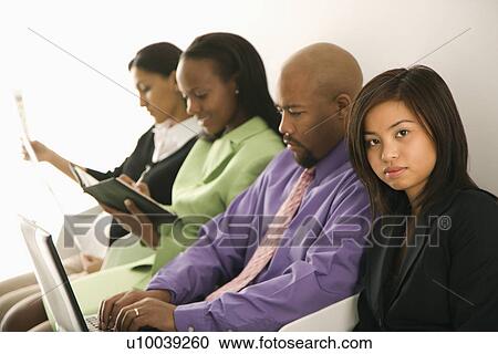 Stock Image - Vietnamese businesswoman sitting looking at viewer with others in background.. Fotosearch