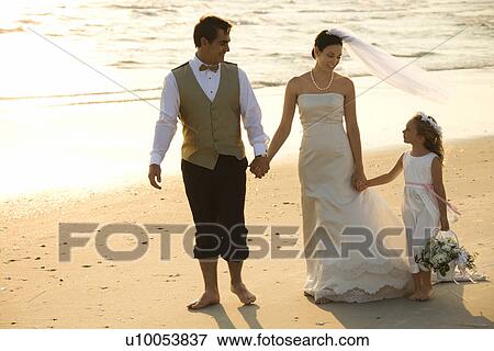 Stock Photo - Bride and groom with flower girl walking barefoot on beach. Fotosearch