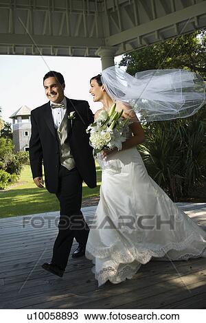 Stock Image - Caucasian mid-adult bride and groom walking together.. Fotosearch