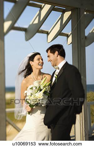 Stock Image - Caucasian mid-adult bride and groom looking at each other talking and laughing.. Fotosearch