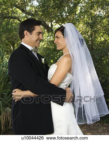 Stock Photograph - Caucasian mid-adult bride and groom embracing, smiling and looking at each other.. Fotosearch